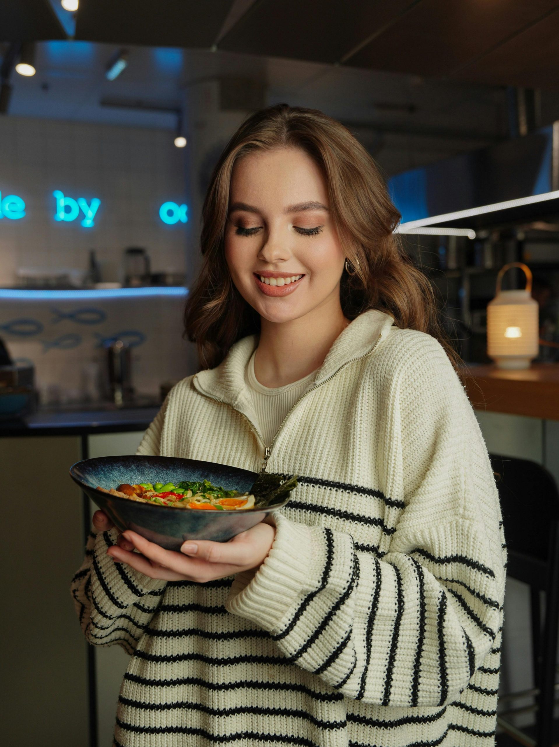 Smiling young woman holding a bowl of salad in a cozy restaurant setting.